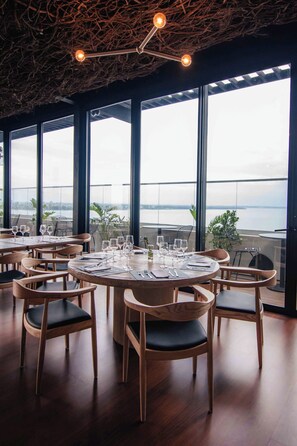 En restaurang med runda bord, stolar och utsikt över vattnet.