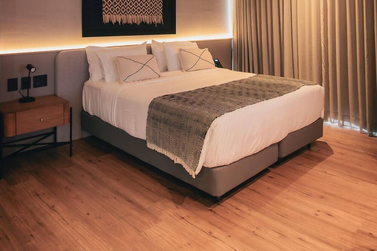A modern bedroom with a large bed, a bedside table, a wall-mounted artwork, and a window with curtains.