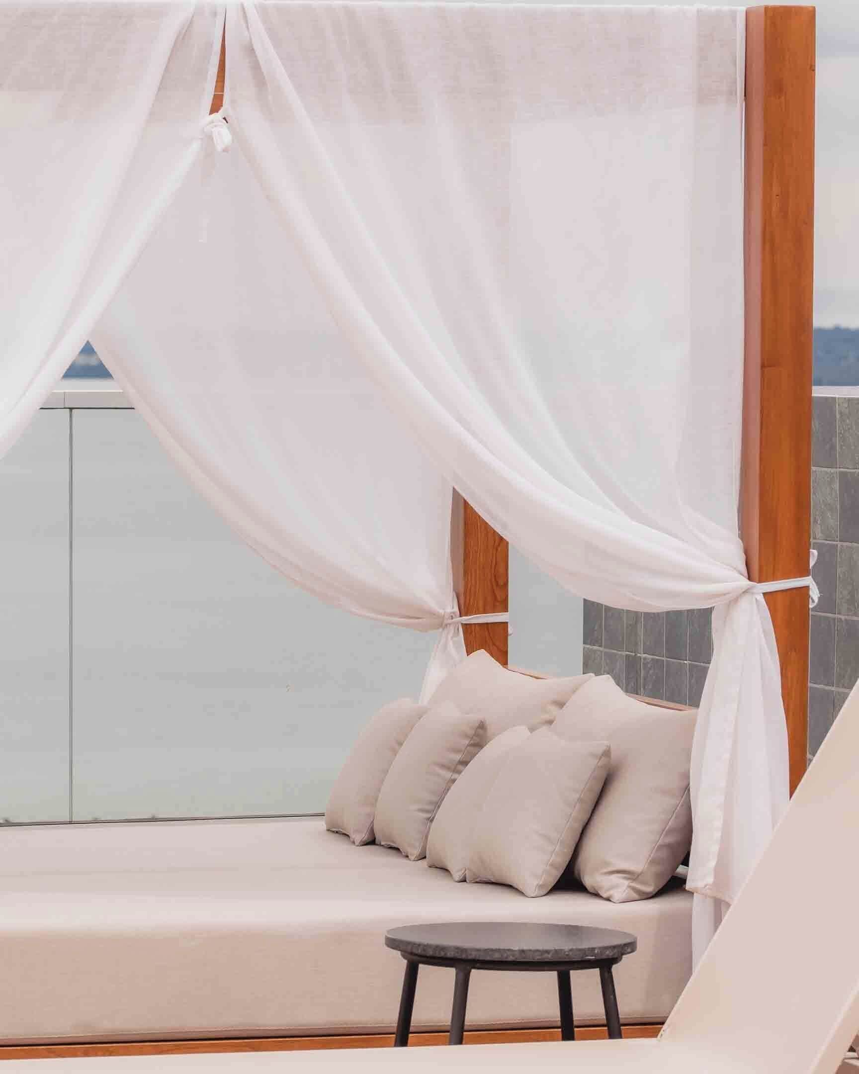 A balcony with a white canopy, a cushioned seating area, and a small round table.