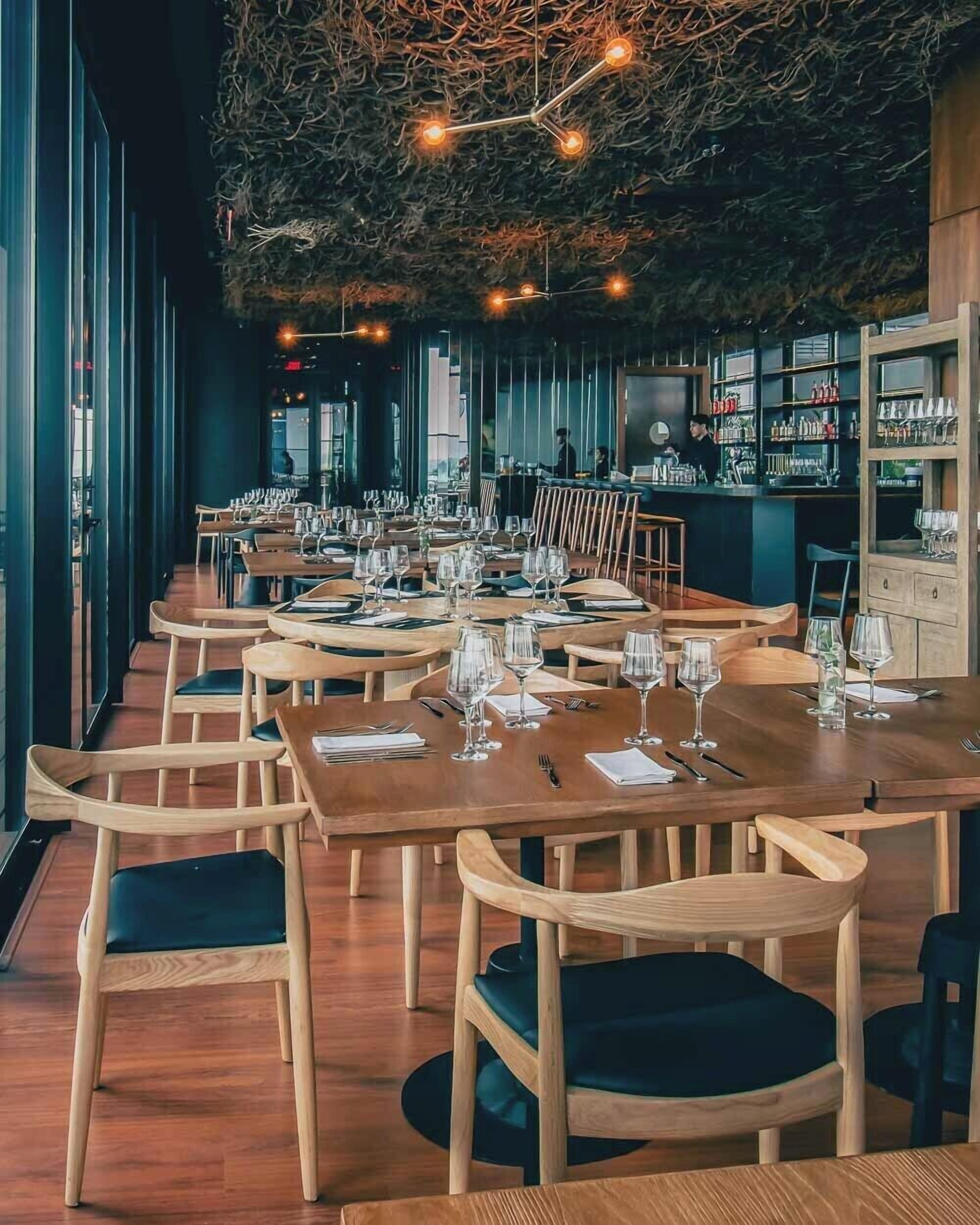 A restaurant interior with long wooden tables, chairs, and a bar area.