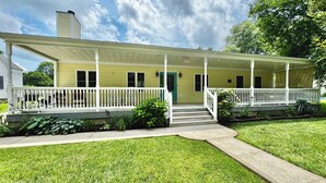 Una casa amarilla con porche, barandillas blancas y una puerta verde.