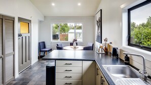 Een moderne keuken met een centraal eiland, een eethoek met stoelen, een groot raam en uitzicht op groen.