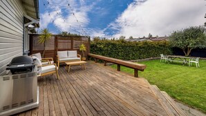 Een houten terras met tuinmeubilair, een barbecue en een picknicktafel.