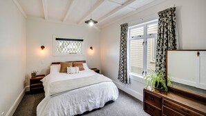 Een slaapkamer met een bed, nachtkastjes, een dressoir, een raam met gordijnen en een plafondventilator.