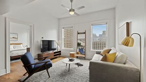Ein modernes Wohnzimmer mit Sofa, Sessel, Couchtisch, Fernseher und Deckenventilator.