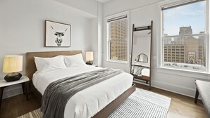 Ett modernt hotellrum med en stor säng, utsikt över staden, ett inramat konstverk på väggen och ett sidobord med en lampa.
