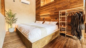 A bedroom with a wooden headboard, a bed with white linens, a potted plant, and a wooden wardrobe with clothes hanging. - Villa SCALA (Sumoto)