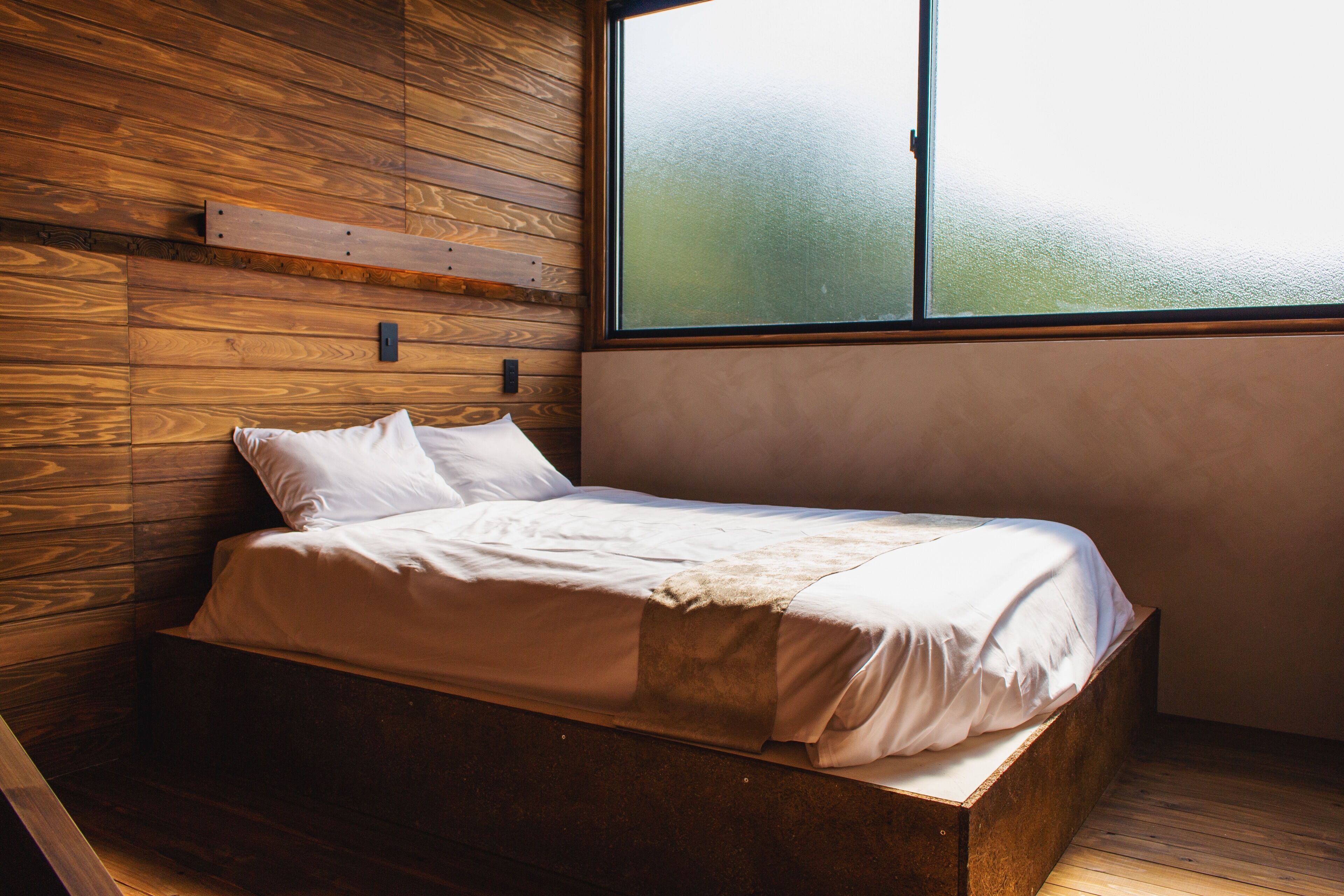 A single bed in a room with wooden panel walls and a large window.