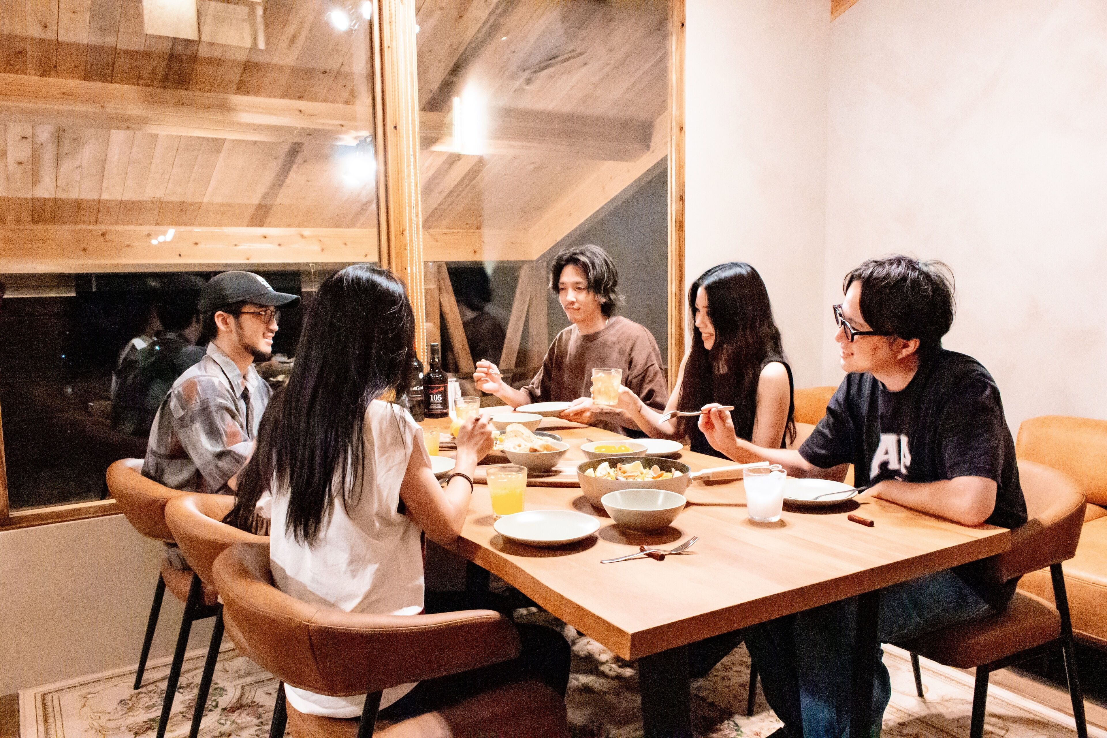 A group of people dining at a wooden table in a room with a sloped ceiling and large windows.
