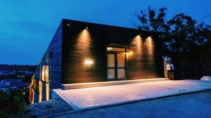 A modern house with a sloped roof, large windows, and a well-lit entrance. - Villa SCALA (Sumoto)