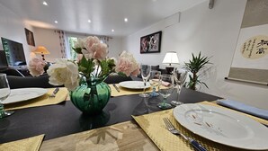 Un comedor con una mesa dispuesta para cuatro, con un jarrón verde con flores, manteles individuales dorados y cristalería transparente.