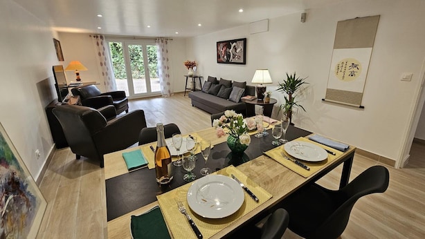 Un comedor con una mesa dispuesta para cuatro, un sofá, un televisor y una ventana con cortinas.