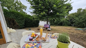Un espacio al aire libre con comedor, mesa preparada para el desayuno, incluyendo cruasanes, fruta y jugo.