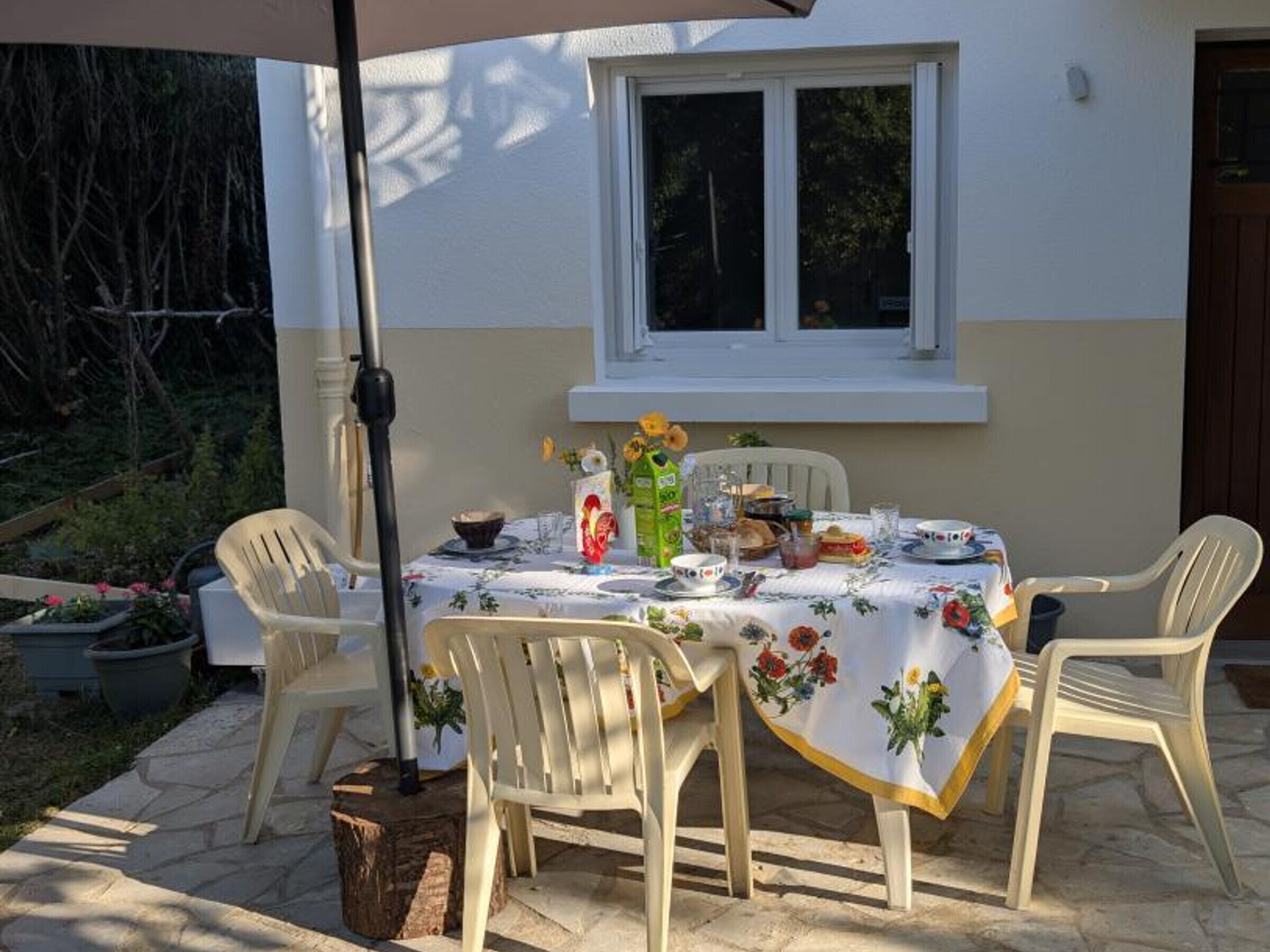 Une terrasse extérieure avec une table dressée pour un repas, entourée de chaises, et une fenêtre au-dessus.