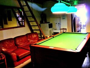 A pool table with a green felt surface, a red leather sofa, and a wooden chair.