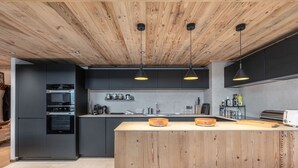 A modern kitchen with wooden ceiling beams, built-in appliances, and pendant lighting.