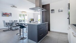 A modern kitchen with a central island, bar stools, a dining area with a table and chairs, and artwork on the walls. - Awesome home in Roquebrune-sur-Argens with WiFi (Roquebrune-sur-Argens)
