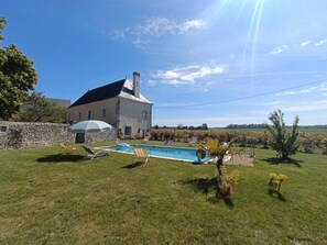 Una casa de piedra con piscina, rodeada de césped y un viñedo al fondo.