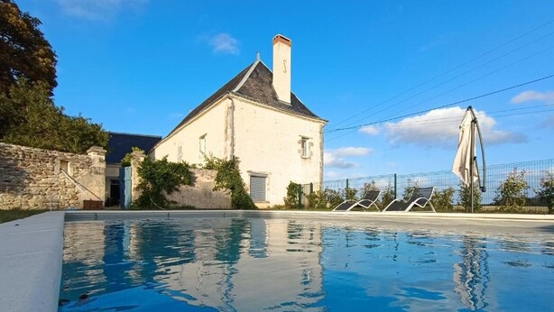 Una piscina con un muro in pietra e un edificio con un camino sullo sfondo.
