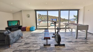 A spacious living area with a foosball table, exercise bike, and a television displaying a sports channel.