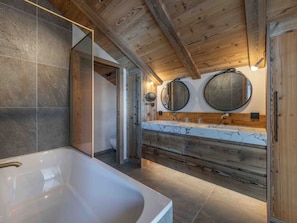 A modern bathroom with a large bathtub, wooden vanity, and two wall-mounted mirrors.