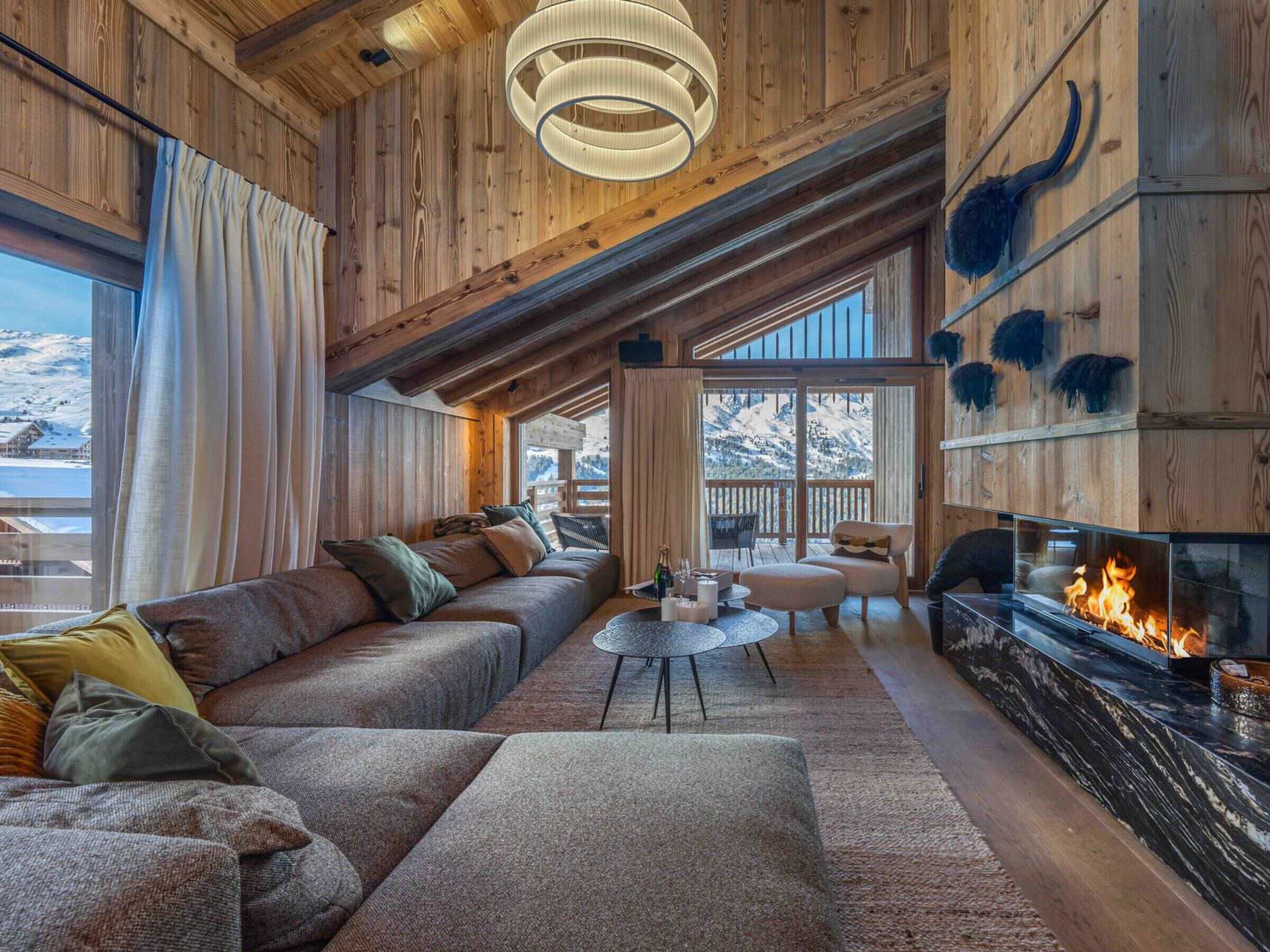 A cozy log cabin interior with a fireplace, a sofa, a dining table, and a view of the snowy landscape.