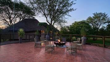 An outdoor patio with tiled flooring, wicker furniture, a fire pit, and a thatched-roof building.