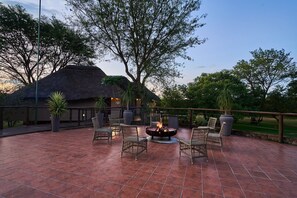 An outdoor patio with tiled flooring, wicker furniture, a fire pit, and a thatched-roof building.