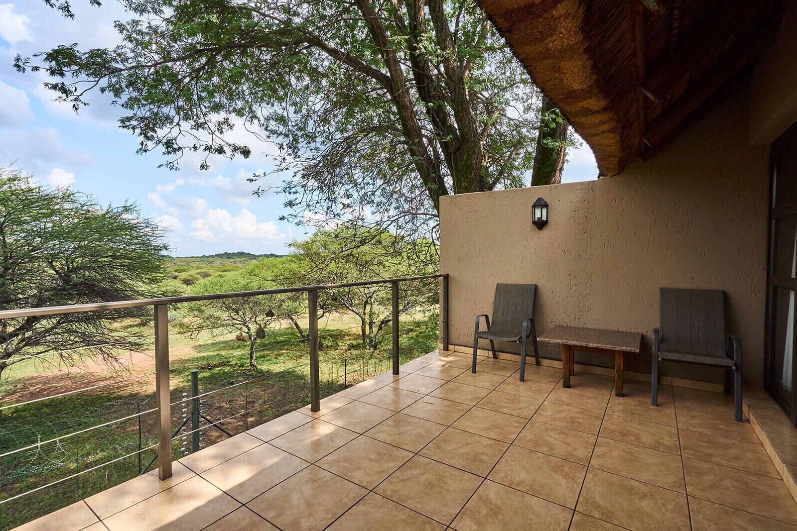 A balcony with two chairs, a table, and a view of a grassy landscape with trees.