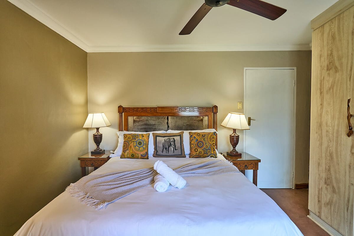 A hotel room with a bed, two bedside lamps, a ceiling fan, and a door.
