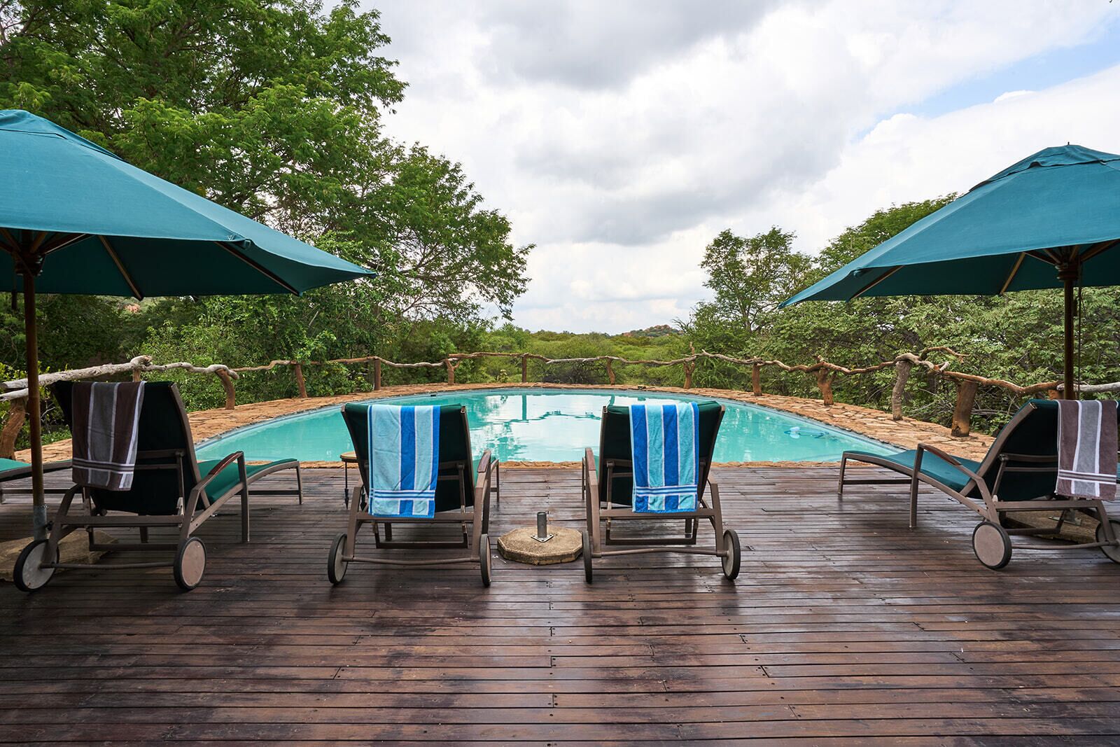 Eine Holzterrasse mit Liegestühlen und Sonnenschirmen mit Blick auf einen Swimmingpool.