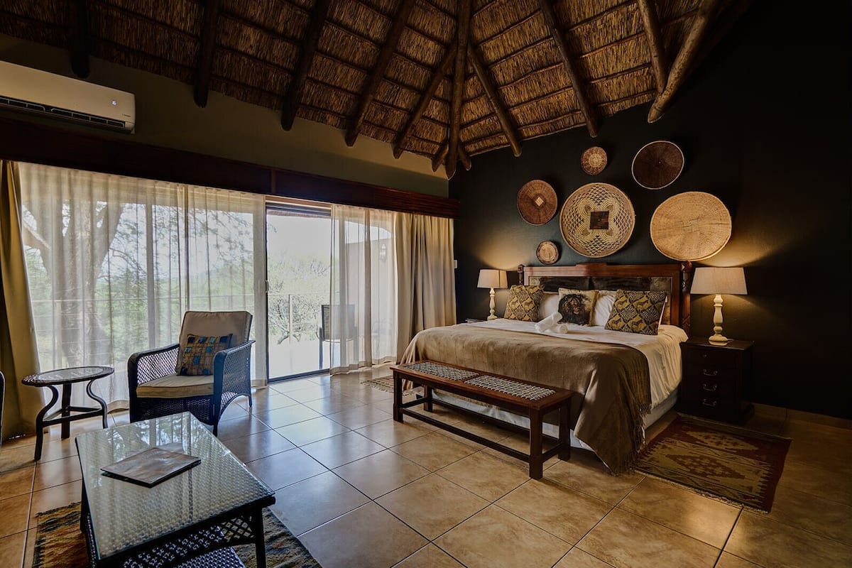 A hotel room with a bed, a chair, a table, a bench, and a view of the outdoors.