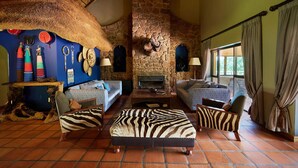 A rustic interior with stone walls, a fireplace, and a seating area with patterned cushions. - Sable Ranch Thaba Khaya (Brits)
