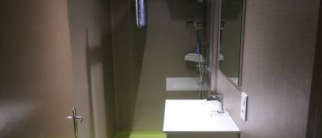 A small bathroom with a white sink, a mirror, and a shower area.