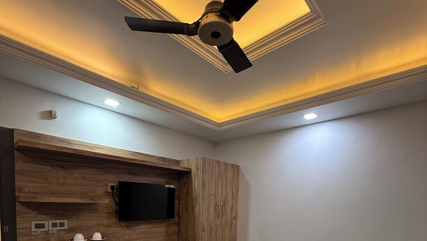 A hotel room with a bed, a wooden vanity, a ceiling fan, and a flat-screen TV.