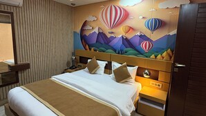 A hotel room with a bed, a ceiling fan, a nightstand, a dresser, and a wall mural. - Hotel Lotus (Kanpur)