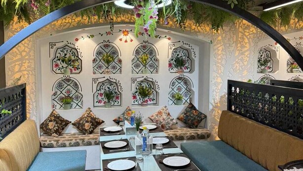 An indoor dining area with a table set for four, surrounded by cushioned seating, and decorated with hanging plants and wall art. - Hotel Lotus (Kanpur)
