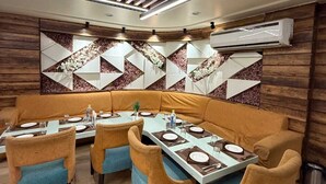 A modern dining area with a long table and cushioned chairs, a decorative wall, and an air conditioning unit.