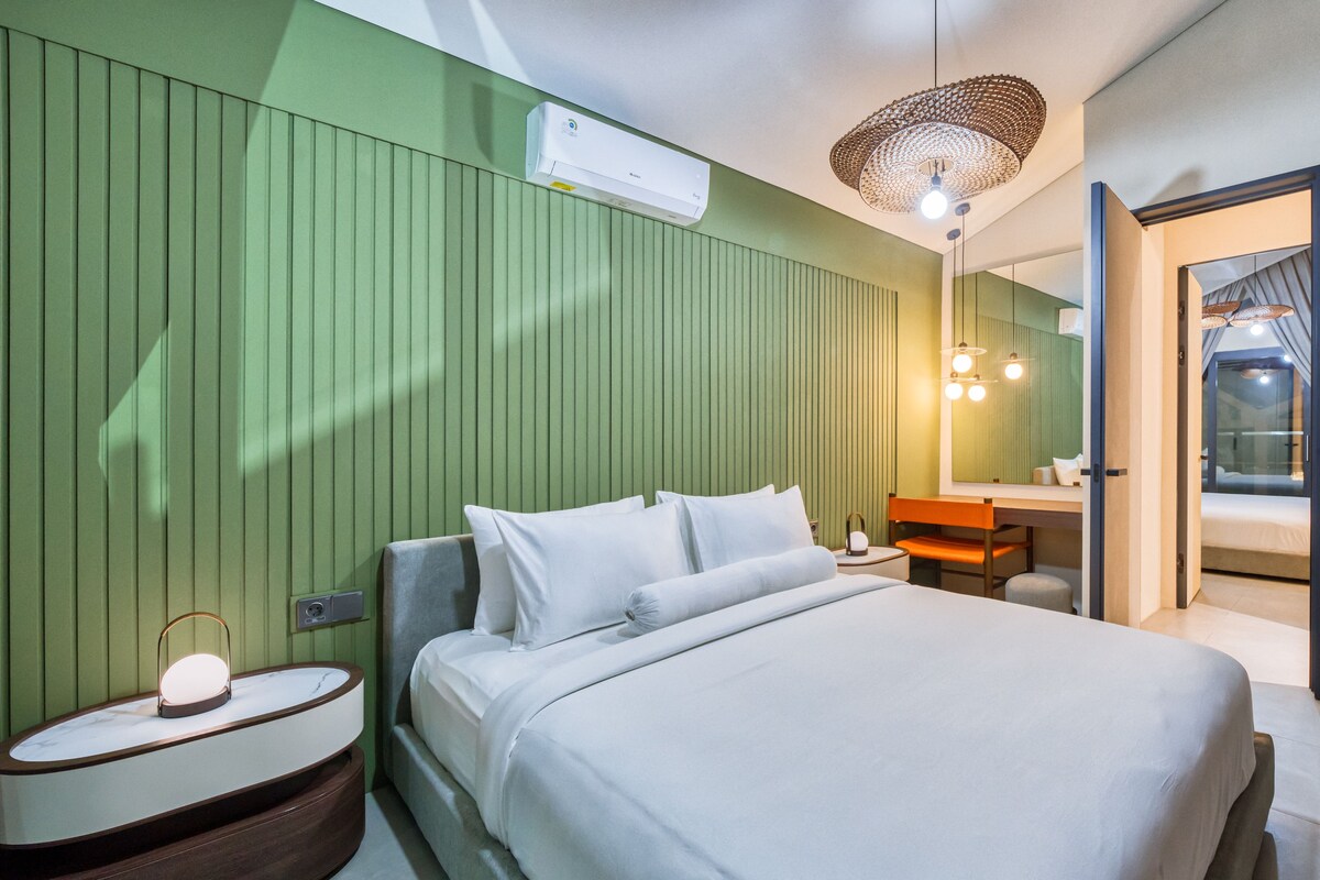 A modern hotel room with a bed, bedside table, and a mirror.