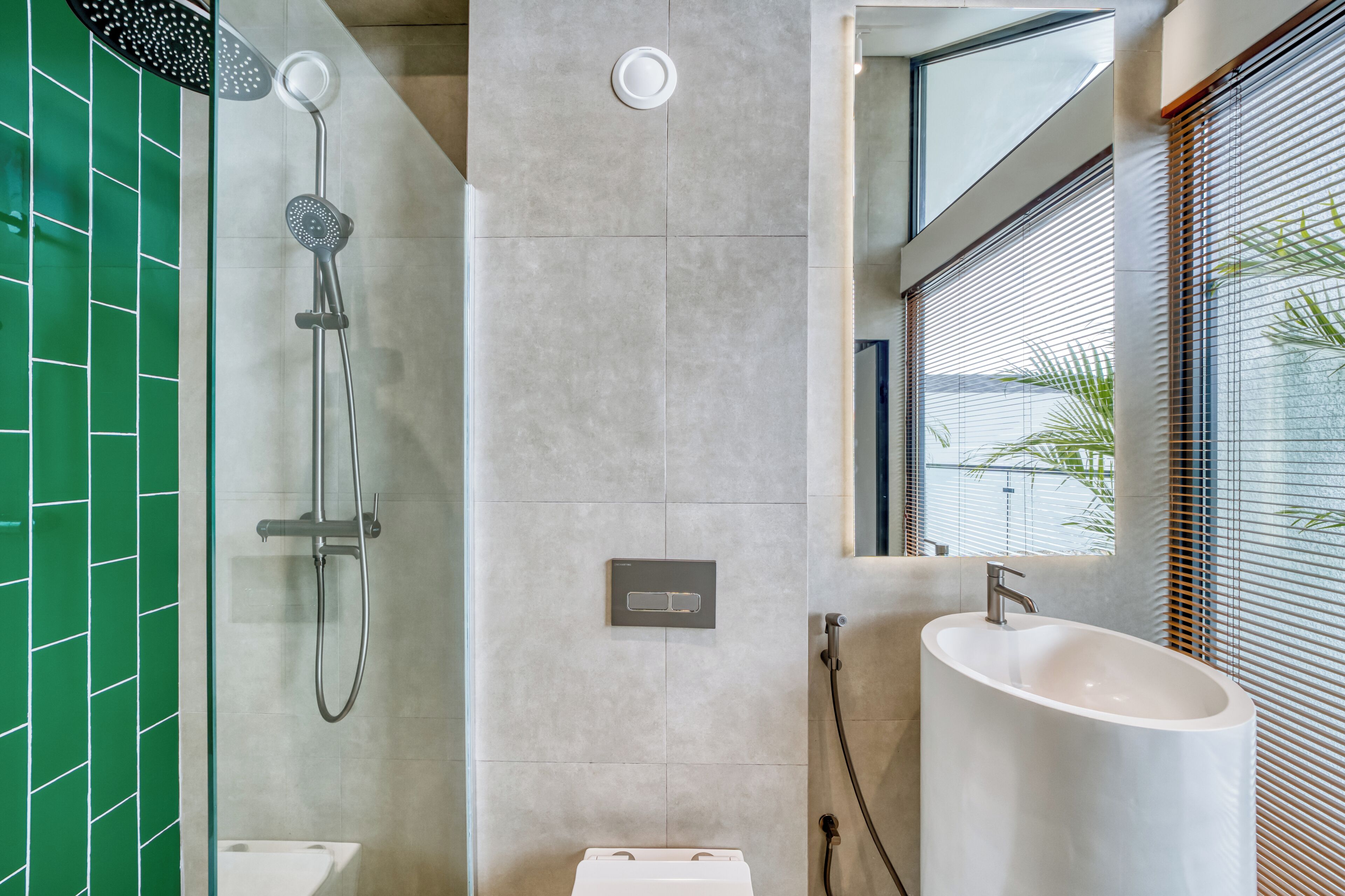 A modern bathroom with a glass-enclosed shower, a white sink, and a green-tiled wall.