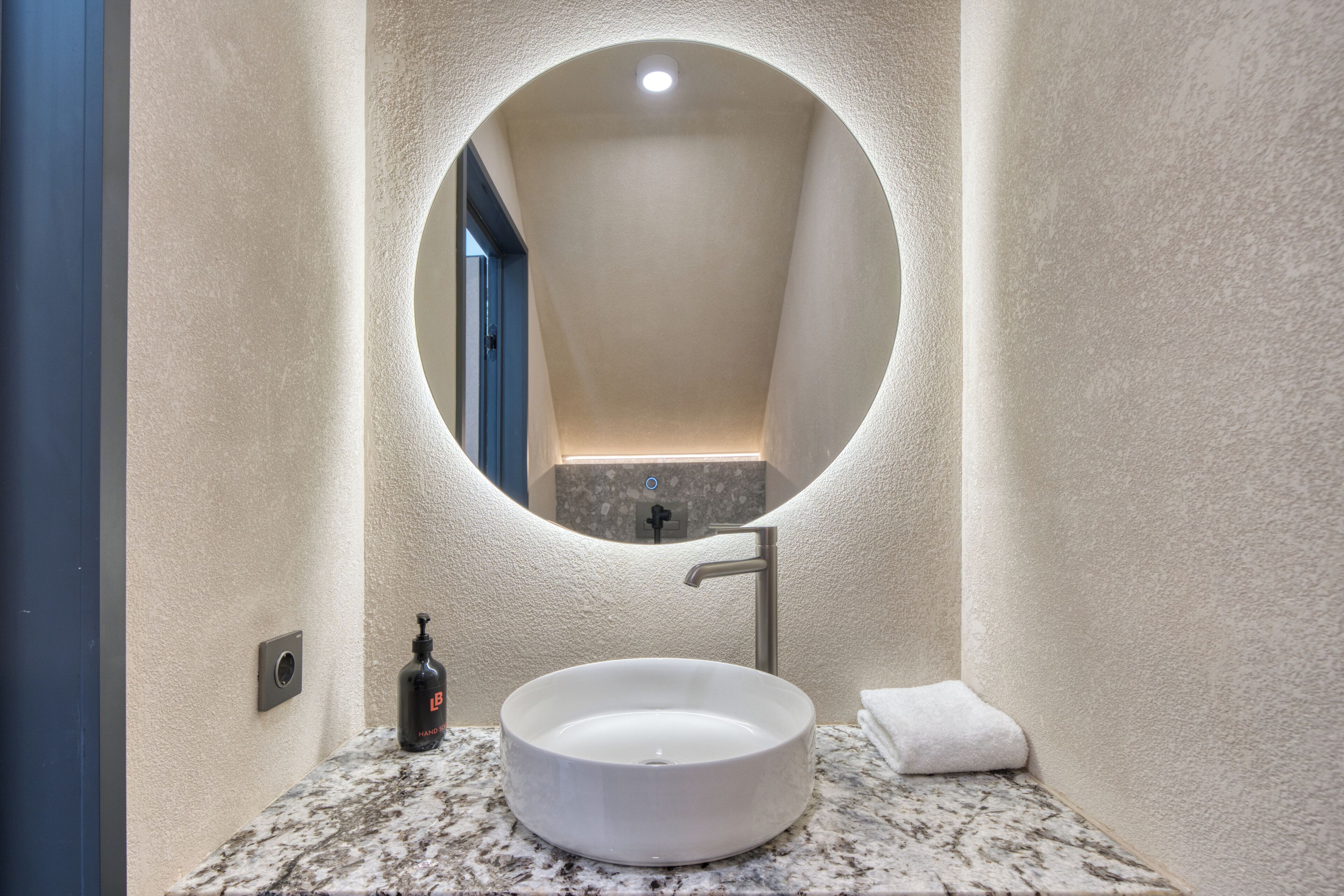 Une salle de bain avec un miroir rond, un lavabo blanc et une serviette posée sur le comptoir.