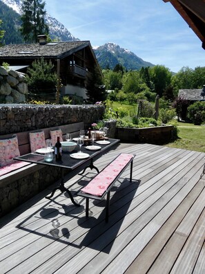 A wooden deck with a table set for dining, stone walls, and a mountain view. - Refugium Draudes with mountain view (Les Houches)