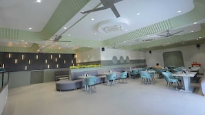 A modern restaurant with a high ceiling, ceiling fans, and a seating area with tables and chairs.