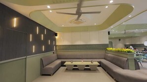 A modern interior with a curved ceiling, recessed lighting, a central seating area, and a kitchen in the background.