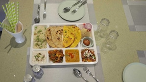 A meal tray with various dishes including rice, flatbreads, and curries, accompanied by cutlery and condiments.