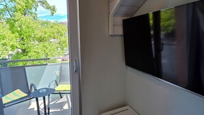 Ein Zimmer mit einer Schiebeglastür, die zu einem Sitzbereich im Freien führt, einem Wand-Fernseher und einer weißen Bank.