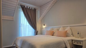 Ein Schlafzimmer mit einem großen Bett, einem Nachttisch, einem Fenster mit Vorhängen und einer geneigten Decke.