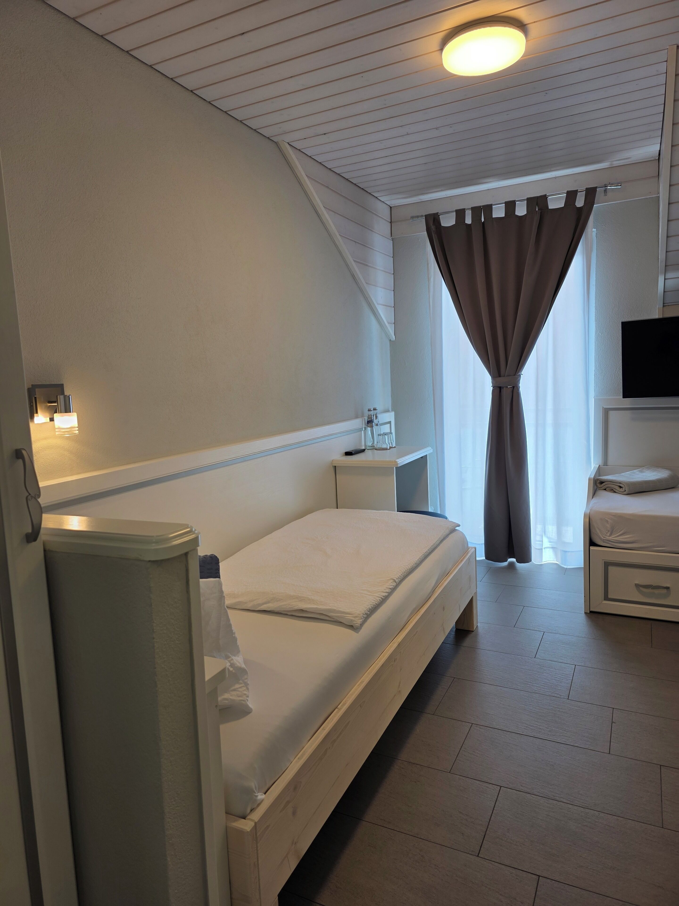 Una habitación de hotel con cama, mesitas de noche, televisor y ventana con cortinas.