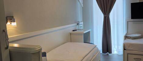 Una habitación de hotel con cama, mesitas de noche, televisor y ventana con cortinas.