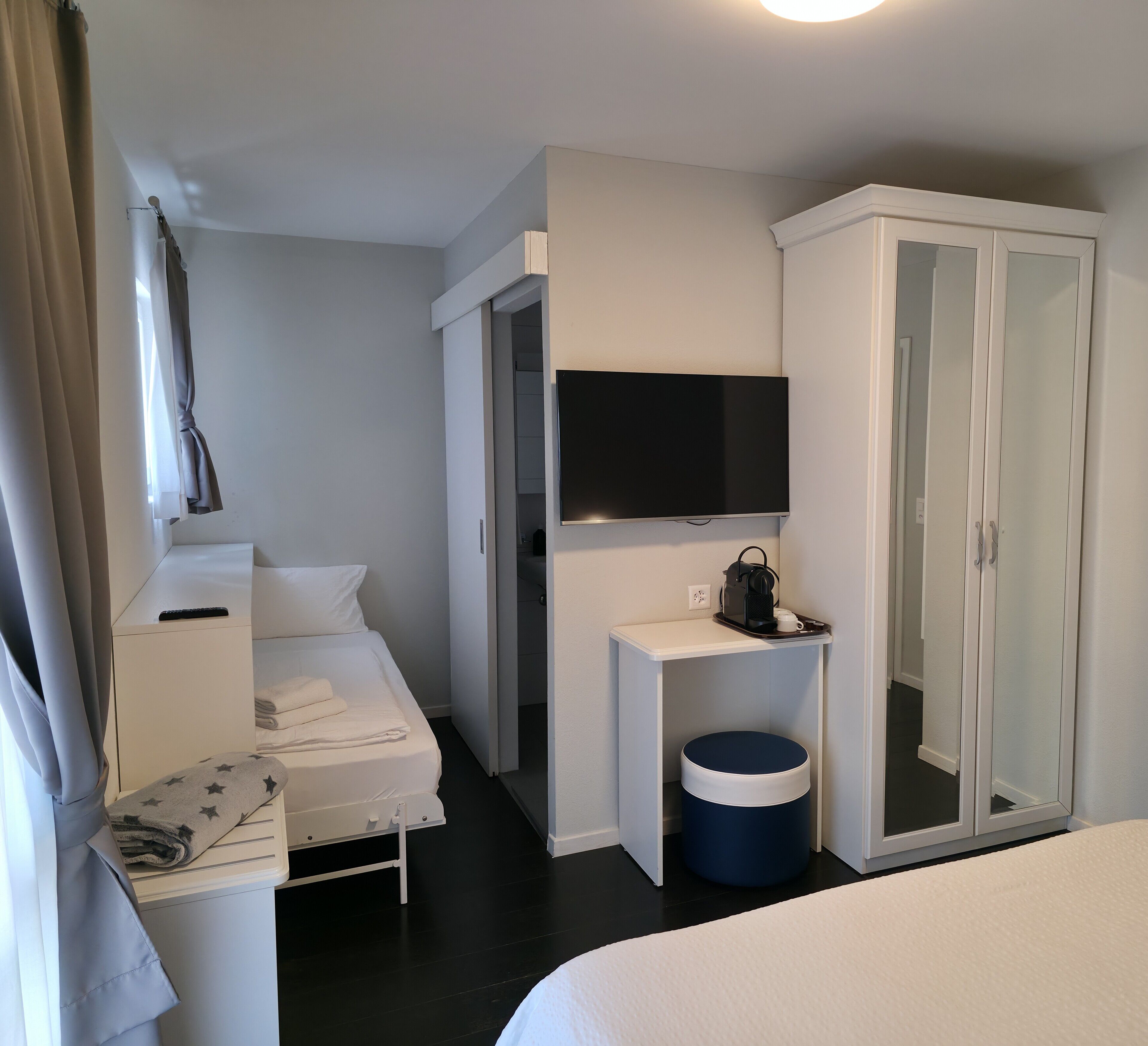 Une chambre d’hôtel comprenant un lit, une table de chevet avec une télécommande, un téléviseur fixé au mur, une armoire et une petite poubelle.
